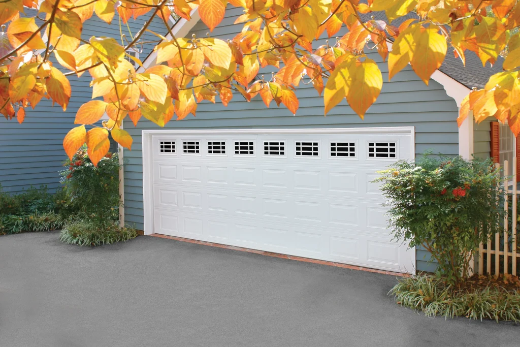 A coastal yellow home features white traditional raised-panel doors with arched sunray windows, providing inspiration for choosing the best garage door design.