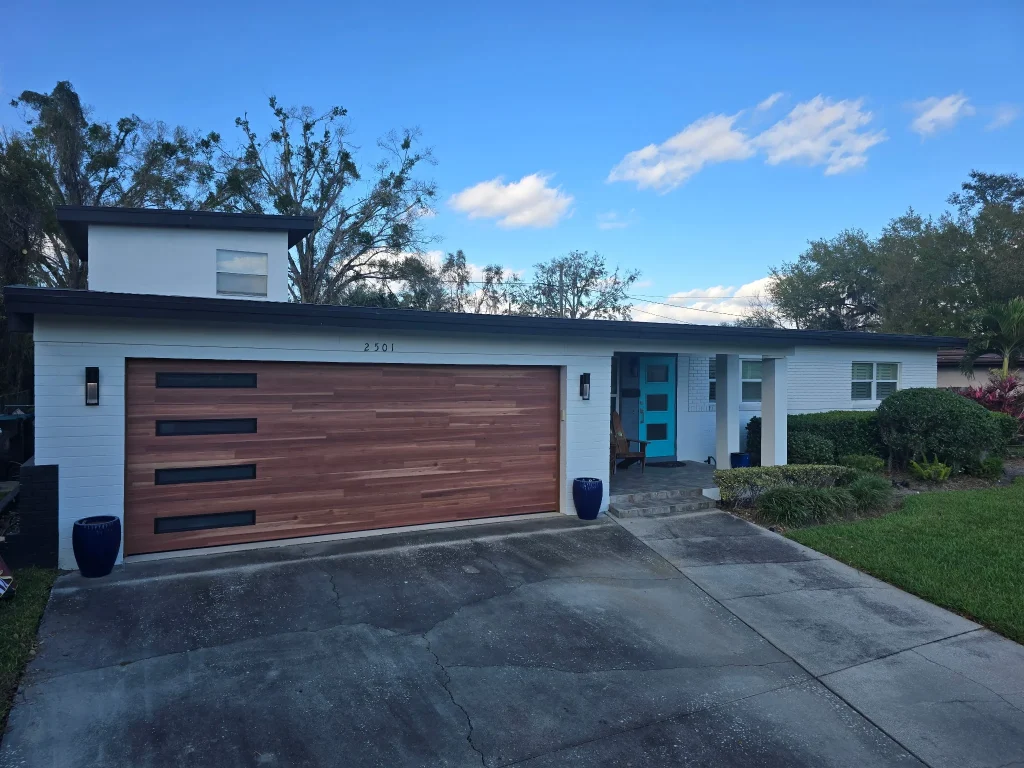 A modern mid-century home features a wood-look door with tinted side windows, showcasing the curb appeal impact of garage door design.