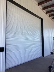 A white corrugated roll-up door with a dark frame is installed on a metal warehouse building, highlighting industrial rolling steel doors.