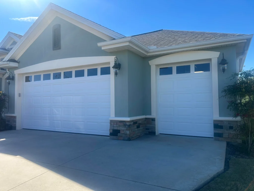 A coastal yellow home features white traditional raised-panel sectional doors with arched sunray windows, providing inspiration when searching for rolling steel doors near me.