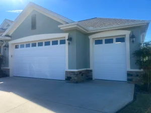 A coastal yellow home features white traditional raised-panel sectional doors with arched sunray windows, providing inspiration when searching for rolling steel doors near me.