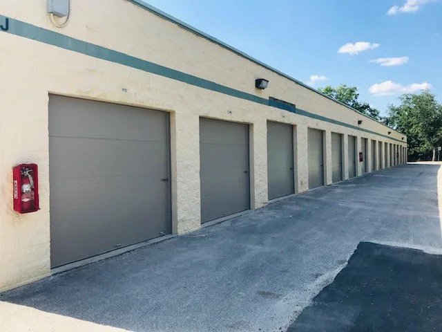 A long row of tan commercial roll-up units along a concrete driveway, providing a visual comparison for selecting right rolling steel door.