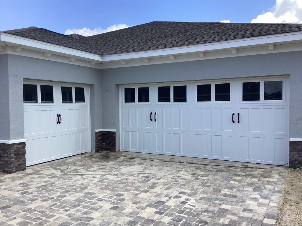 Three white carriage-house style doors with black handles are perfectly aligned on a stone-accented garage, emphasizing the importance of storm-ready door security.