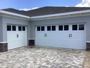 Three white carriage-house style doors with black handles are perfectly aligned on a stone-accented garage, emphasizing the importance of storm-ready door security.