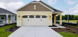 A yellow stucco home features a cream-colored carriage-house style door with arched window grids under an architectural archway, highlighting a beautiful residential garage door in DeLand, FL.
