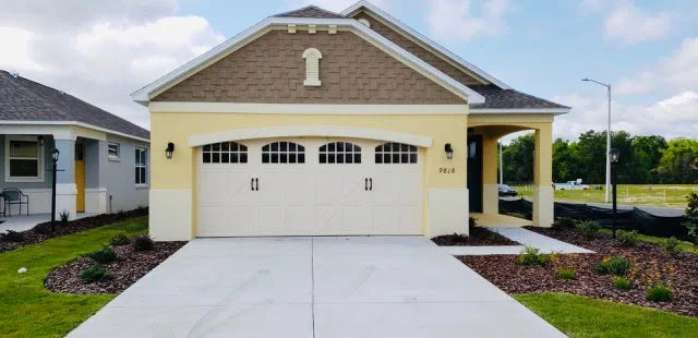 A yellow stucco home features a cream-colored carriage-house style door with arched window grids under an architectural archway, highlighting a beautiful residential garage door in DeLand, FL.